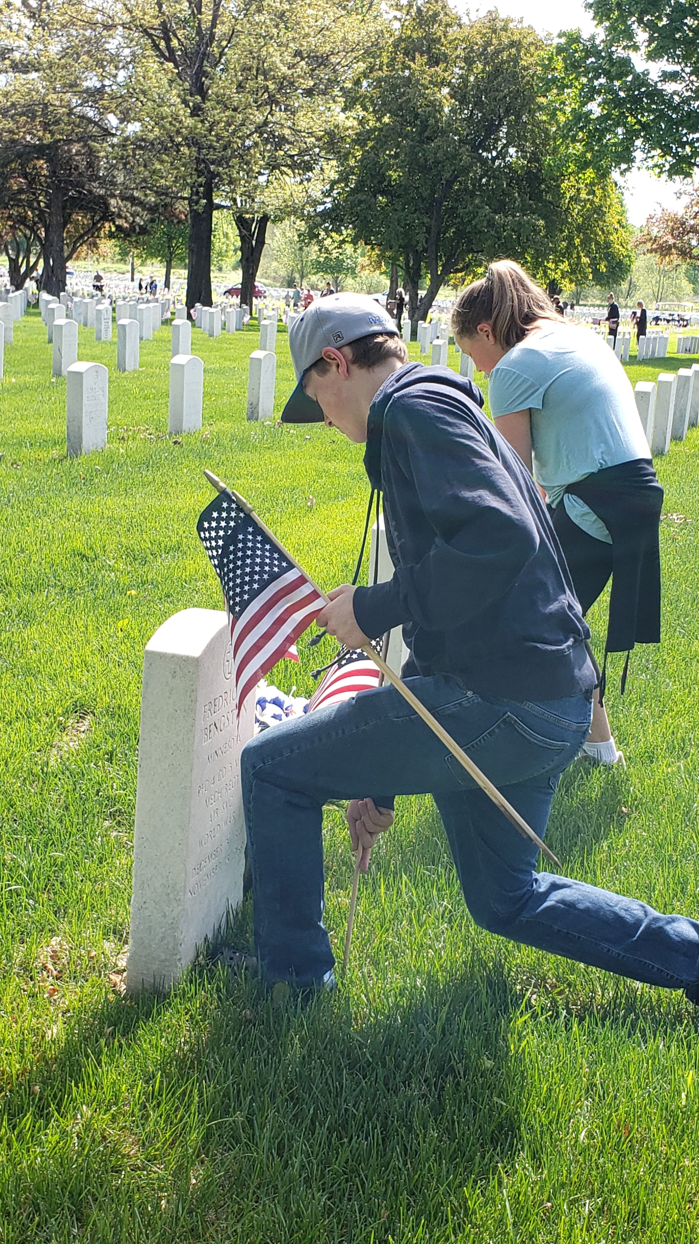 Kids placing flags on headstones at Fort Snelling National Cemetary in Minnesota